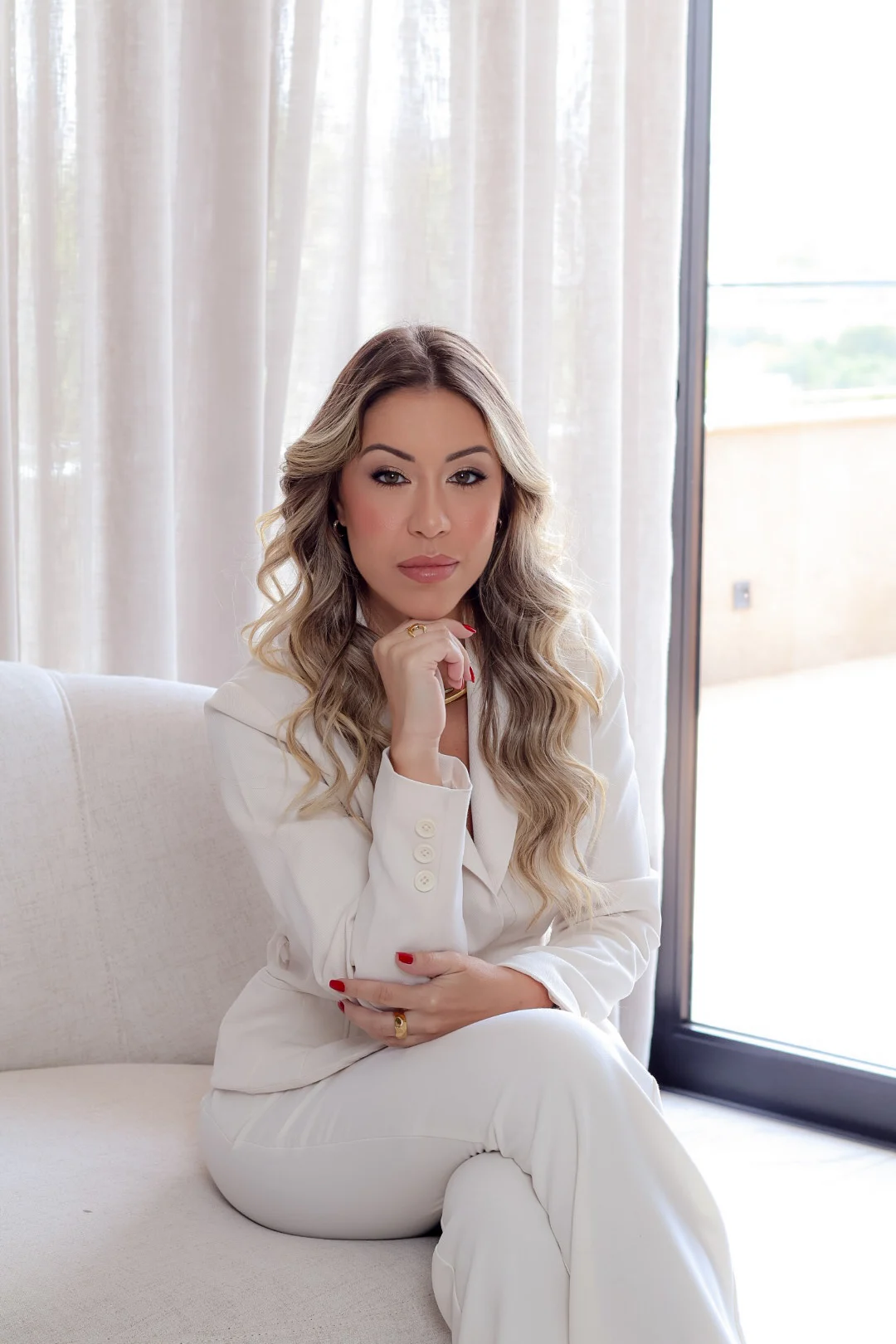 Roberta Peixoto sentada em um sofá, usando um terno claro